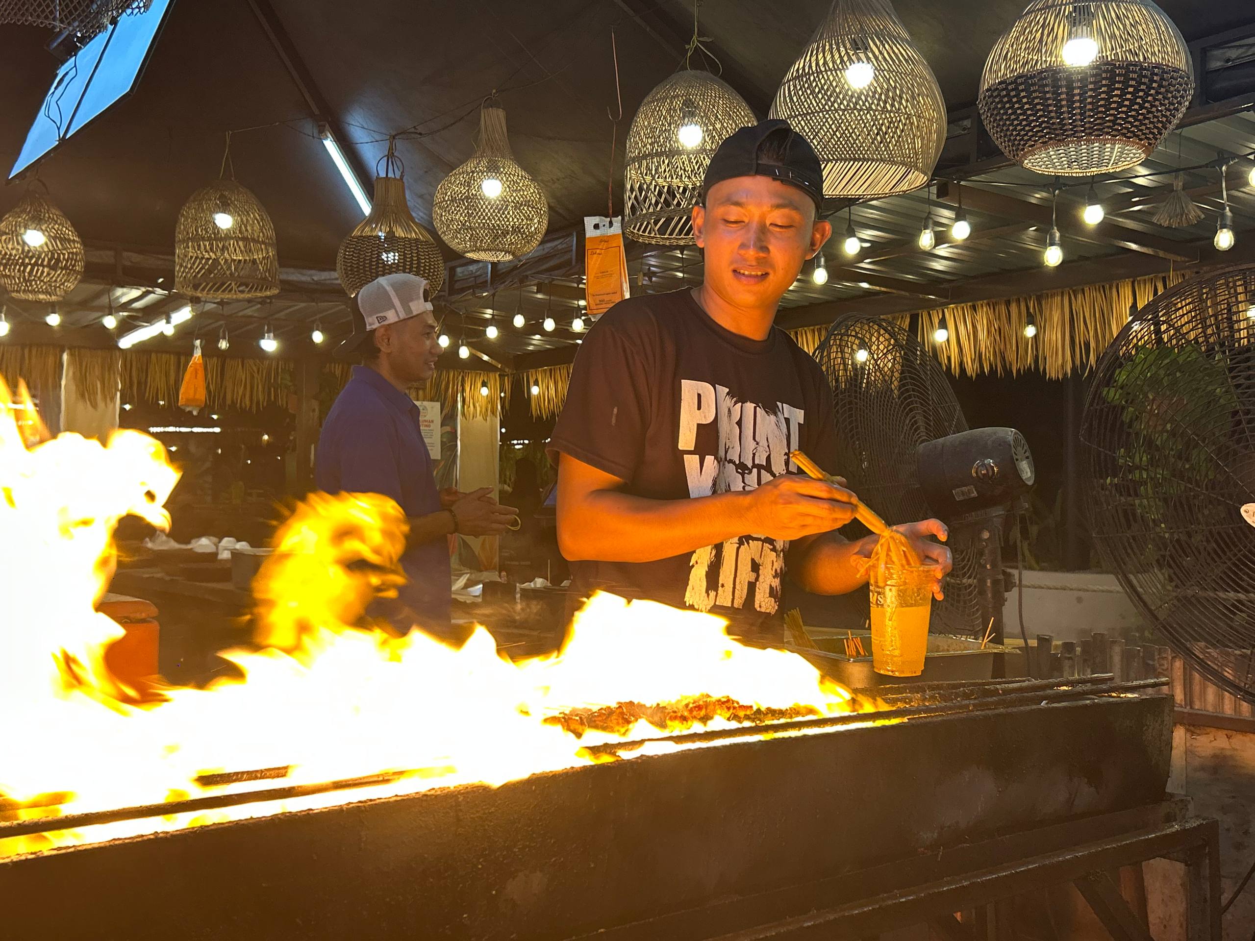 Satay prepared over an open flame beneath woven lanterns